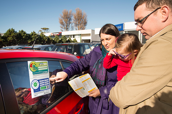 A women, man and child looking at the safety rating label on a car.