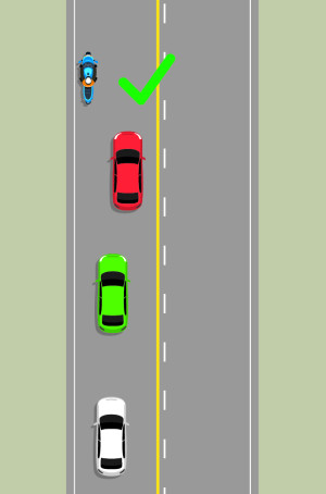 A road with two lanes and four vehicles travelling in the northbound lane. The front blue motorcycle is keeping as close to the left side of the road as possible, allowing the red car behind to pass it.