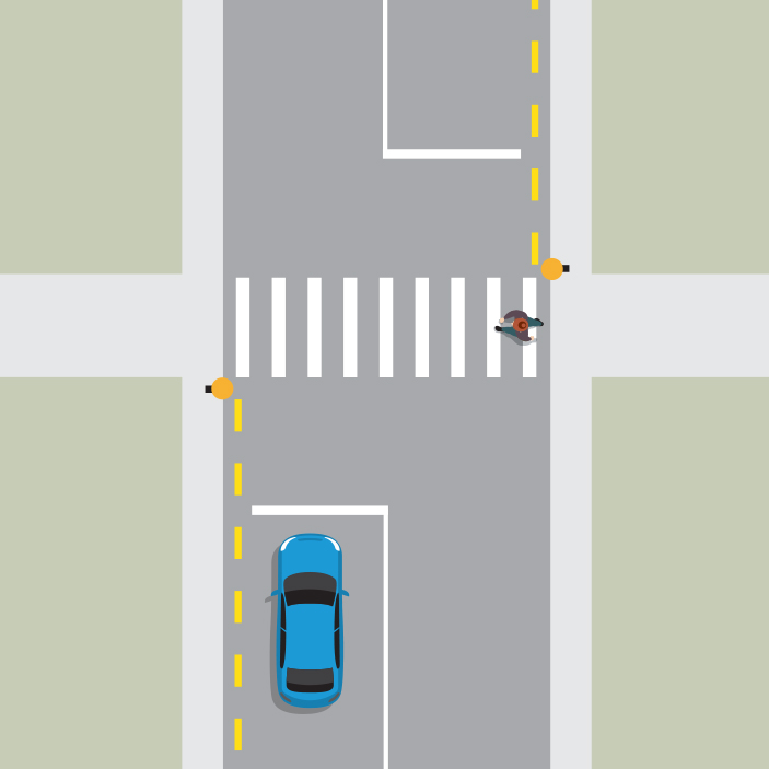 A blue car is stopped behind a white line in front of a pedestrian crossing. A pedestrian is crossing the road.