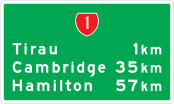 A green rectangle with white border. A red highway shield with the number one sits top and centre, with town names and kilometres listed below.