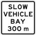 White road sign with black text that says slow vehicle Bay 300m