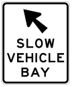 White road sign with a black arrow and text that says slow vehicle bay