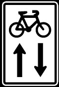 Contra-flow cycle sign with black cycle symbol and two vertical arrows pointing at different directions underneath