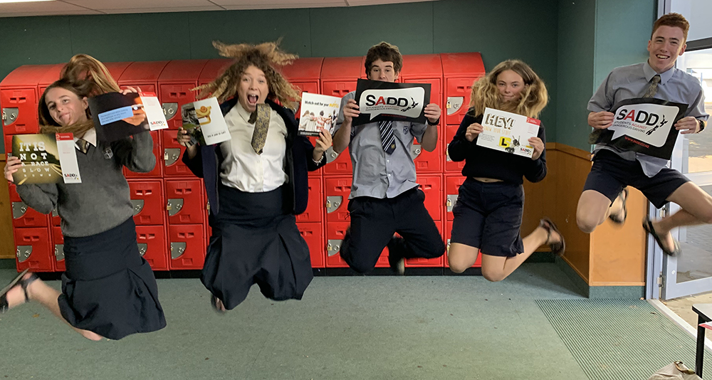 Five school students holding SADD resources and jumping in the air.