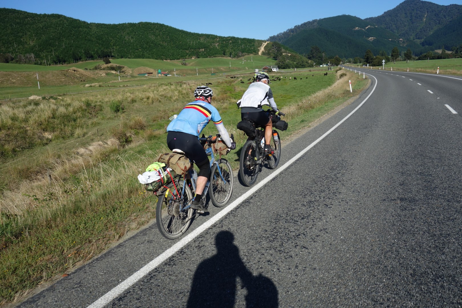 Two cyclists seen from behind riding along a state highway.