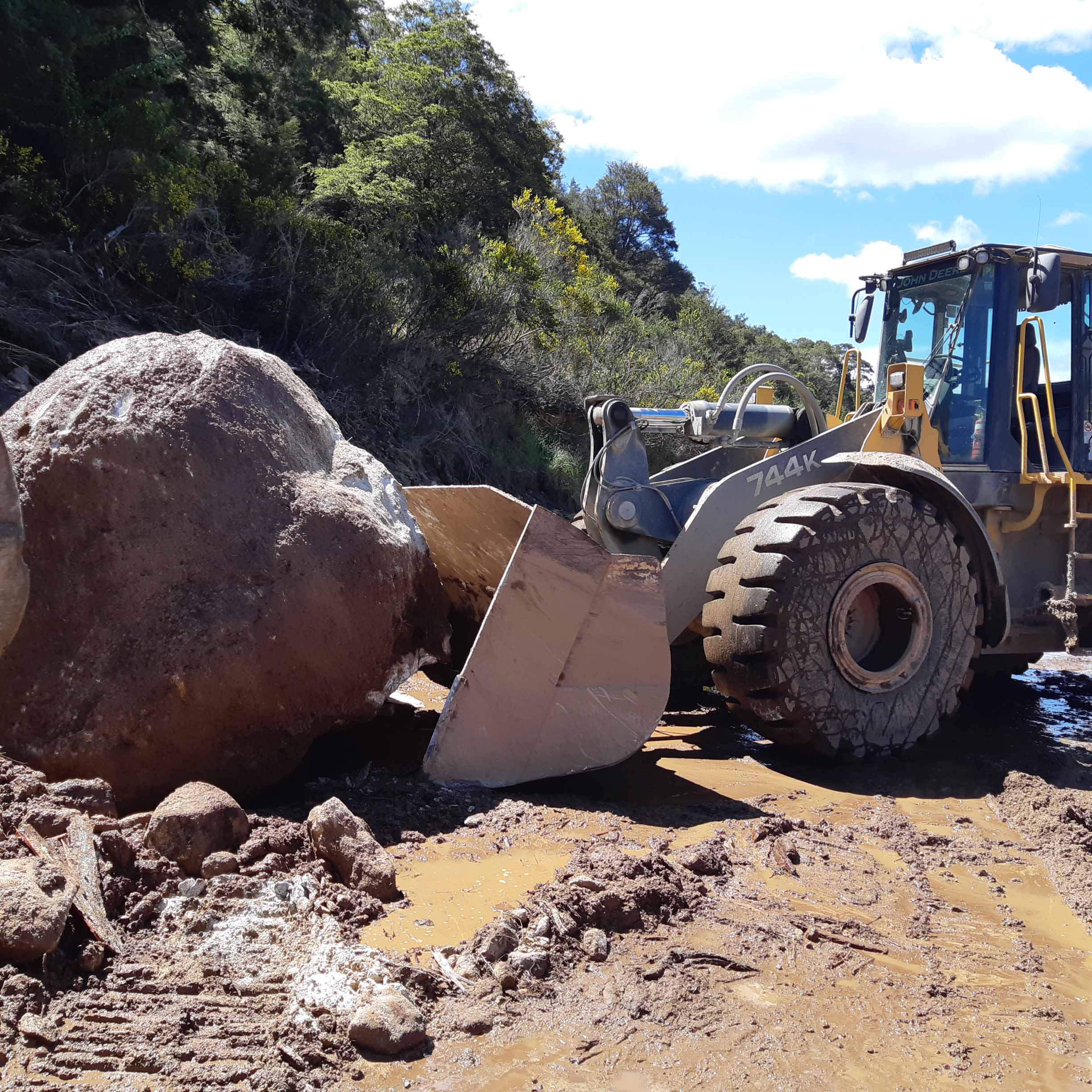 a blue digger attempts to move large rock from slip on SH6 north of Murchison
