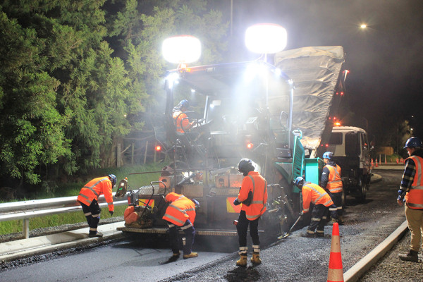 A group of people working at night laying asphalt