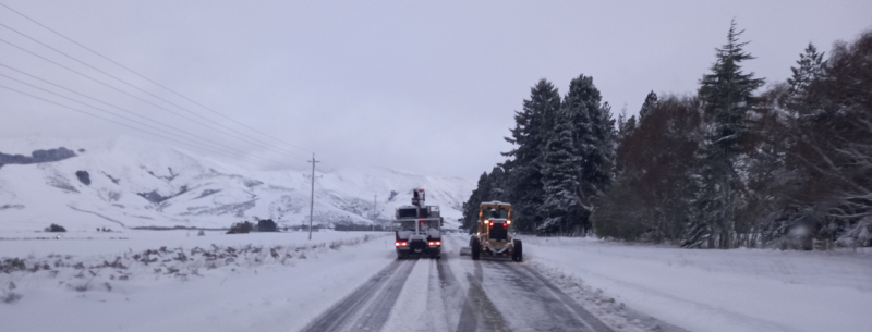 A snow covered landscape with two trucks driving on the road