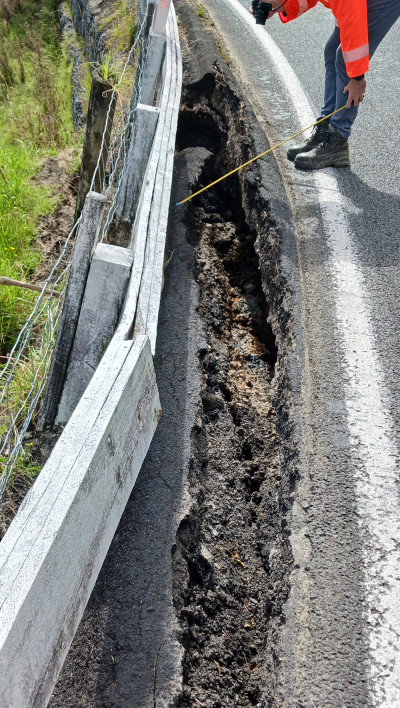 A person measuring a large crack at the side of a road.