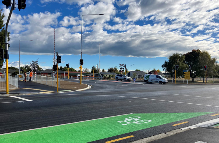 A green bike lane on a busy street with cars and trucks, providing a safe space for cyclists at a new intersection.