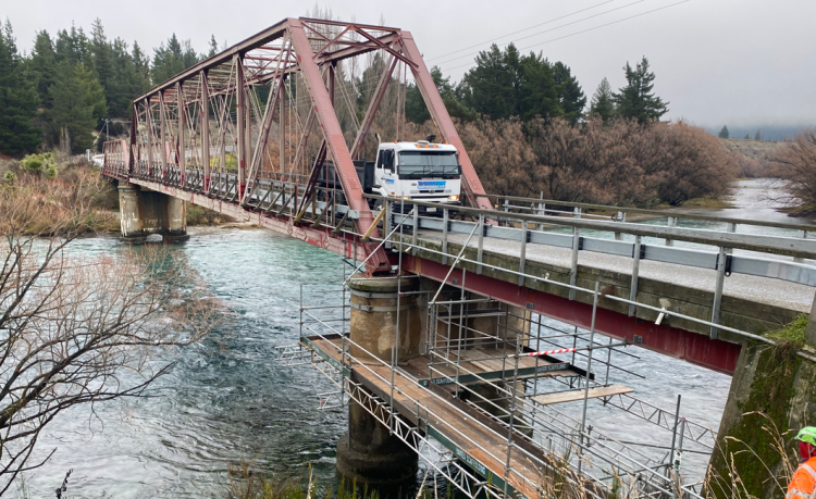 A truck crossing a river on a bridge.