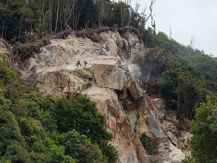 A group of individuals stands on a cliffside, engaged in rock scaling activities.