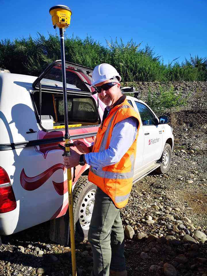 Mark Fleming wearing a high-vis orange vest holding a pole vertically next to a vehicle