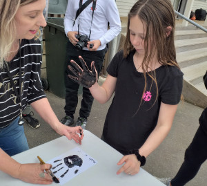 Girl with black paint on her hand making hand prints on paper.