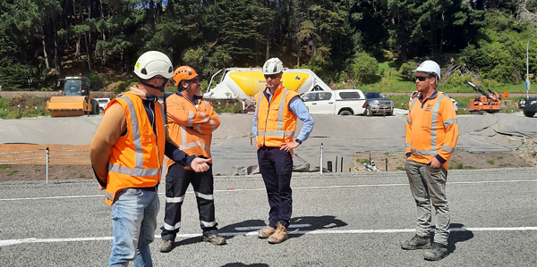 Four men in orange high-vis inspecting newly sealed local accessroad.