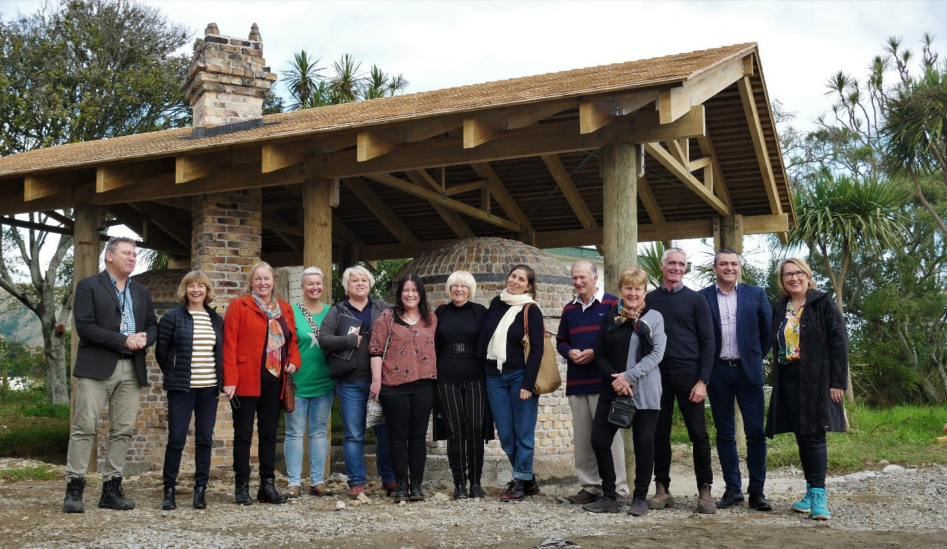 Twelve people standing in front of the relocated Smišek kilns housed under a wooden structure protecting them from the rain.