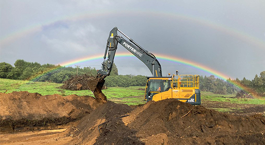 construction machine at work with double rainbow in the background