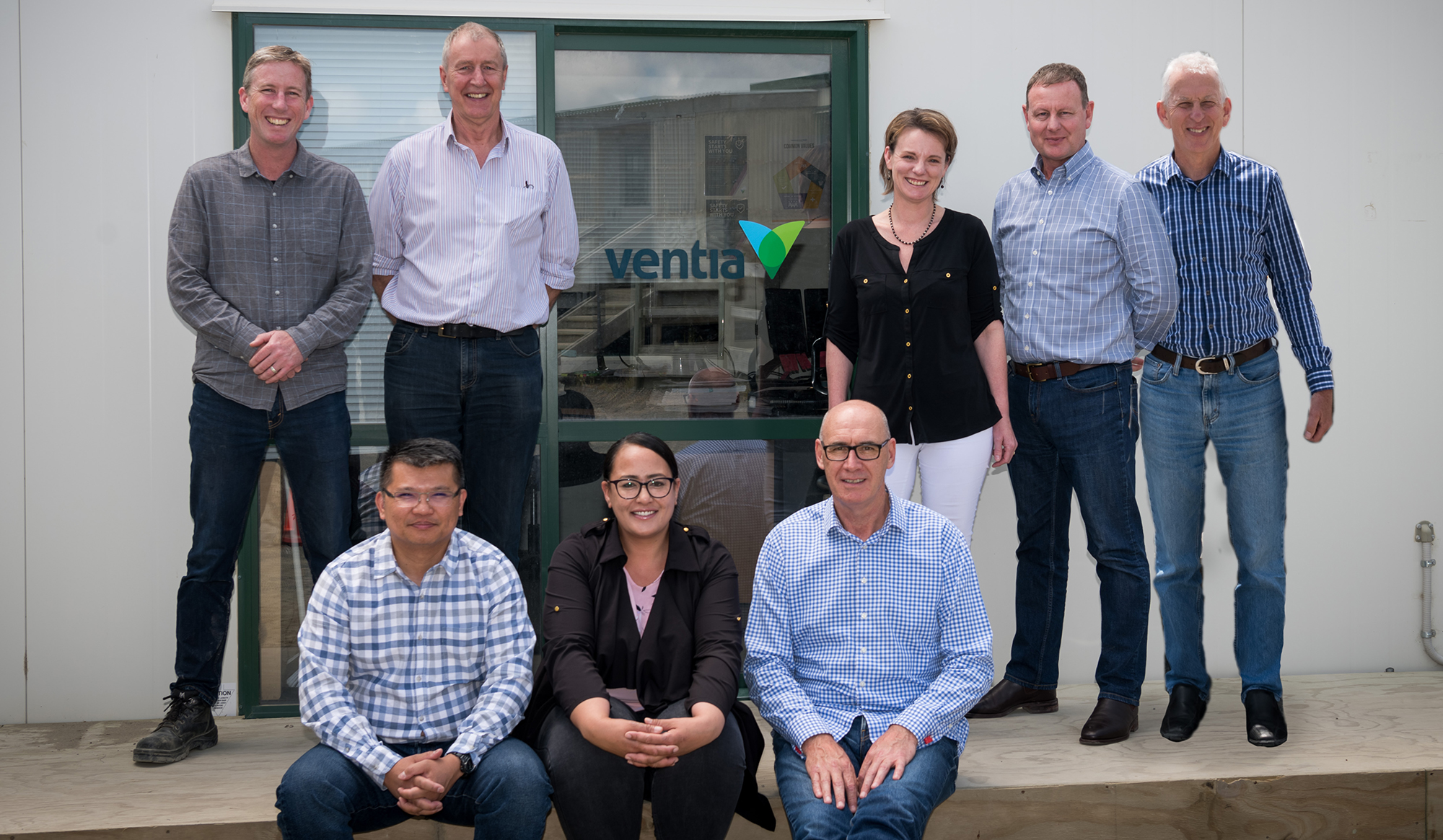 Eight members of the Ventia team standing in front of their project office with the Ventia logo on the glass door.