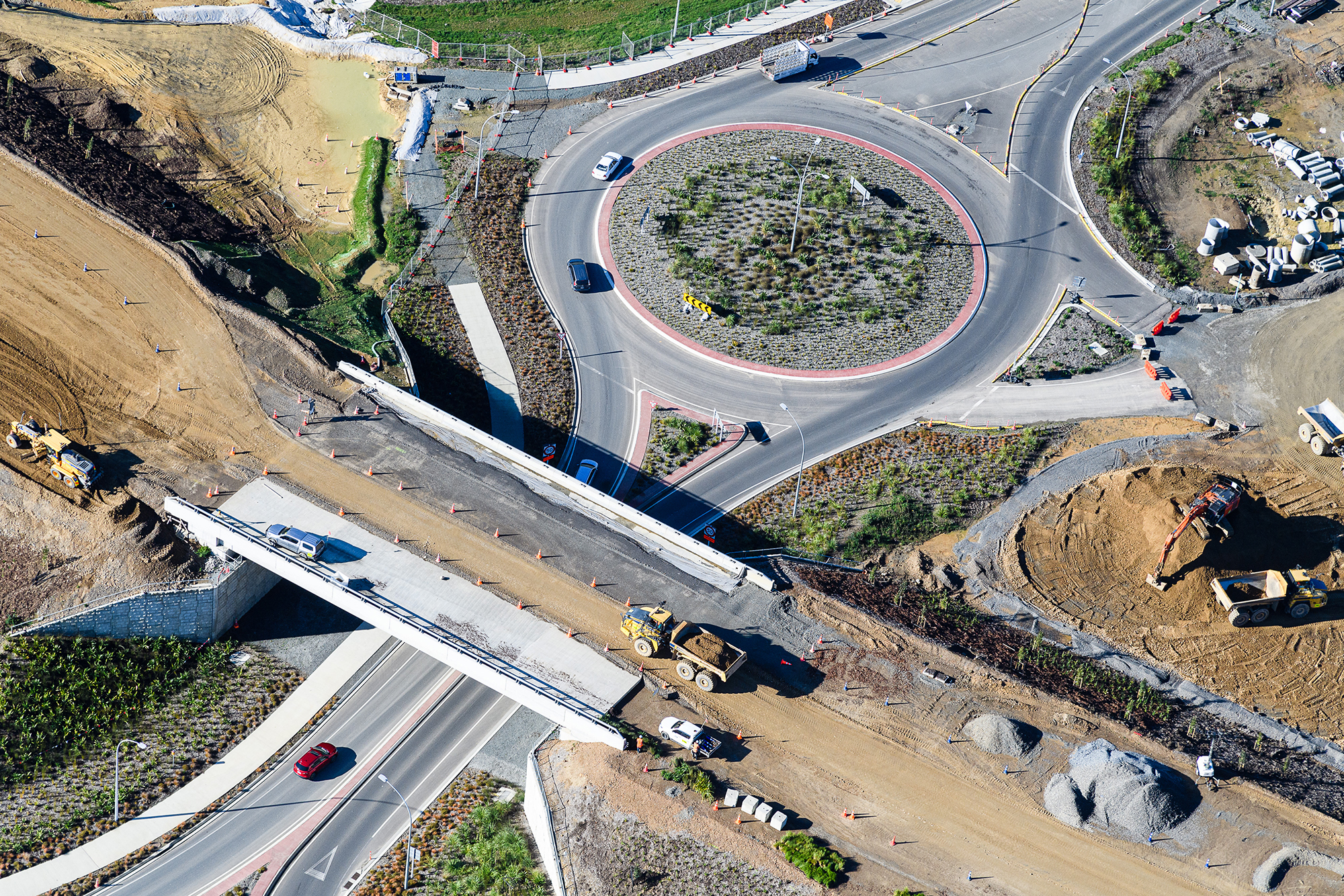 Bridge 13 under construction to the left of roundabout with plantings.