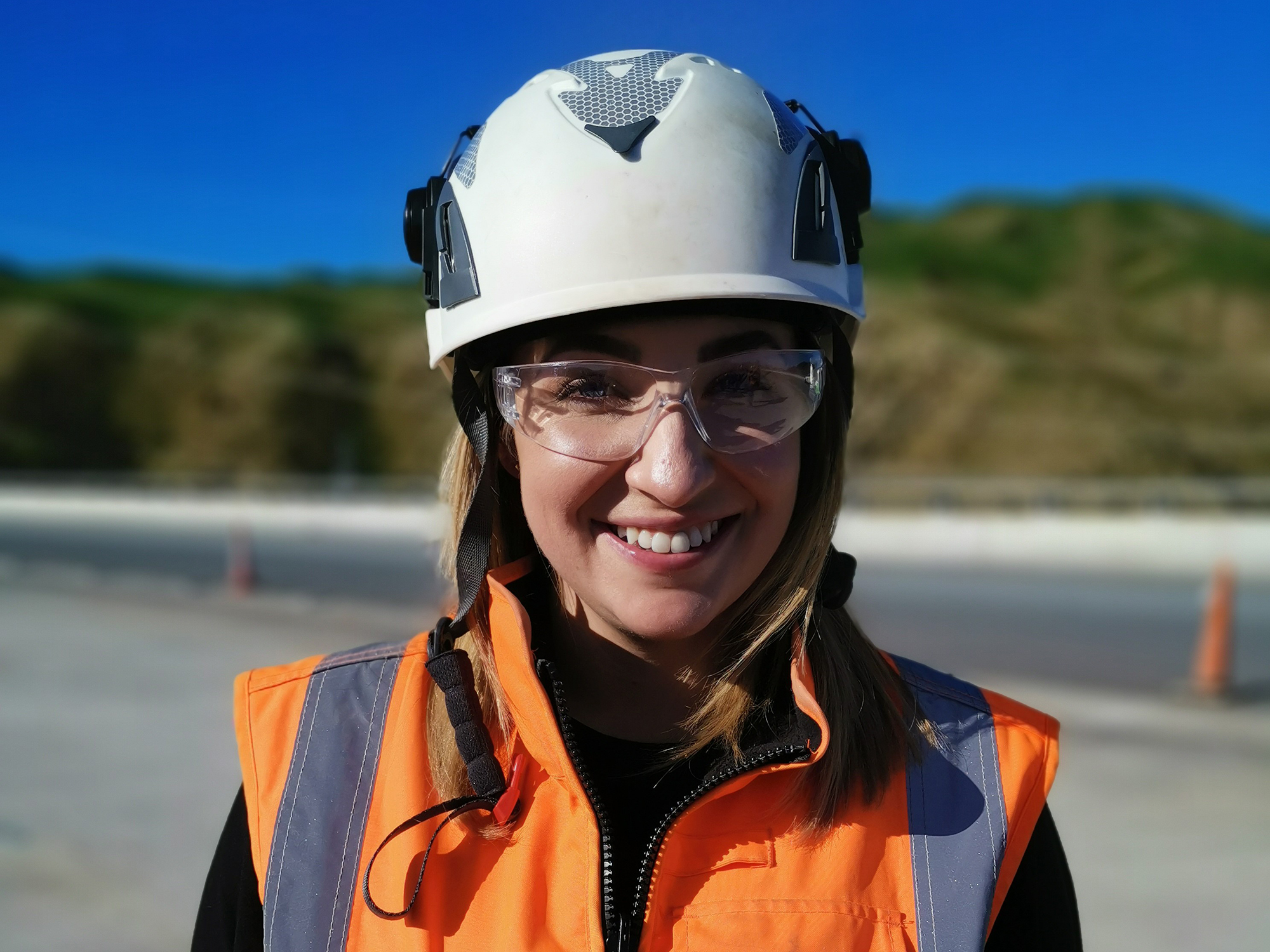 Ellah Black wearing an orange Hi Vis jacket, white helmet and safety glasses.