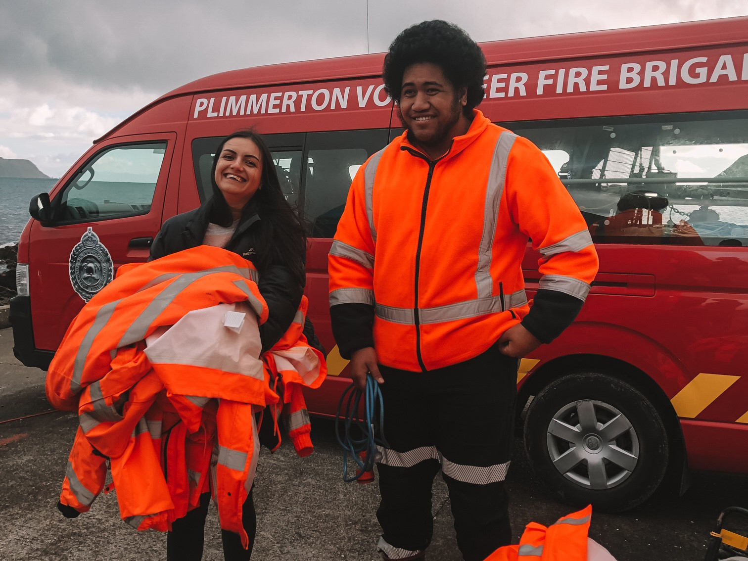 Two people holding and wearing Hi Vis jackets standing in front of Plimmerton Volunteer Fire Brigade van.
