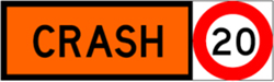 Orange sign with a black border and black text saying crash. Attached to the right is a speed limit sign with a red circle border and black number 20 in the centre.