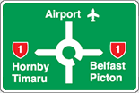 A green rectangle with white border. It has a white circle with vertical and horizontal white cross-shape lines. Red highway shields and town names sit on the left and right. The top points to the words airport and a picture of a plane.