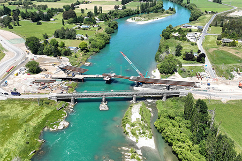 A new bridge under construction across a river, with an existing bridge next to it
