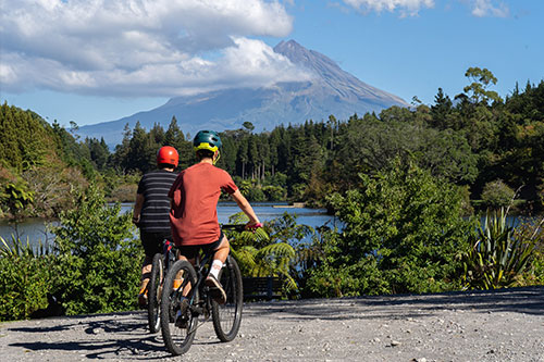 Two cyclists stopping at a scenic lake and Mount Taranaki