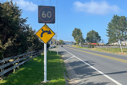road showing 60km flashing sign speed limit and a yellow road sign showing a curved road with an intersection