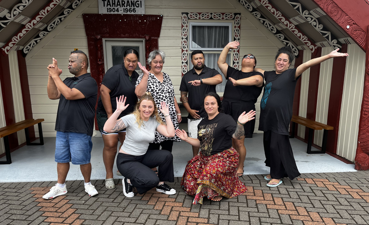 A group of people smiling and posing for a picture outside a marae, capturing a joyful moment together.