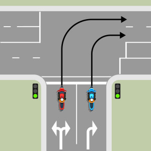 A blue motorcycle and a red motorcycle are waiting to turn right from a one-way street. The blue motorcycle in the right lane must stay in the right lane through the intersection. The red motorcycle in the left lane must stay in the left lane.
