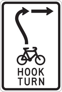 A black and white sign with a bicycle icon in the centre and text below reading hook turn. Above the bicycle an arrow points up and then curves to the right.