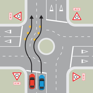 A blue car and a red car are approaching a multi-laned roundabout with four exits. Two black arrows show the cars don't indicate until they are past the exit before the exit they are taking, then they signal left. The cars stay in the same lane.