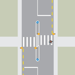 A person is crossing the road from right to left, using a pedestrian crossing with a raised island.