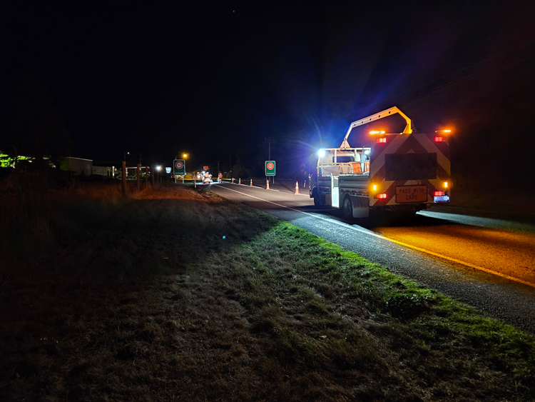 A utlitly truck carrying road signs on the road at night.