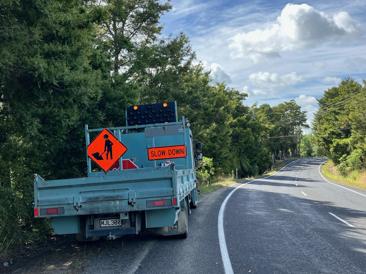 A utlitly truck carrying road signs parked on the shoulder of the road.