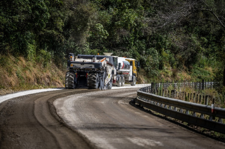 A truck and tractor on a country highway road with  greenery in the background.