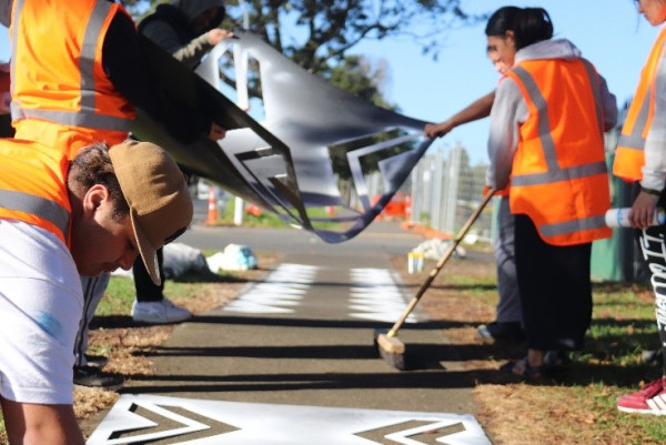 People spray painting geometric patterns on a pedestrian pathway using stencils.