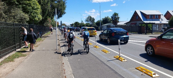 School children cycle down a bike lane separated by cars by temporary raised humps and bollards.