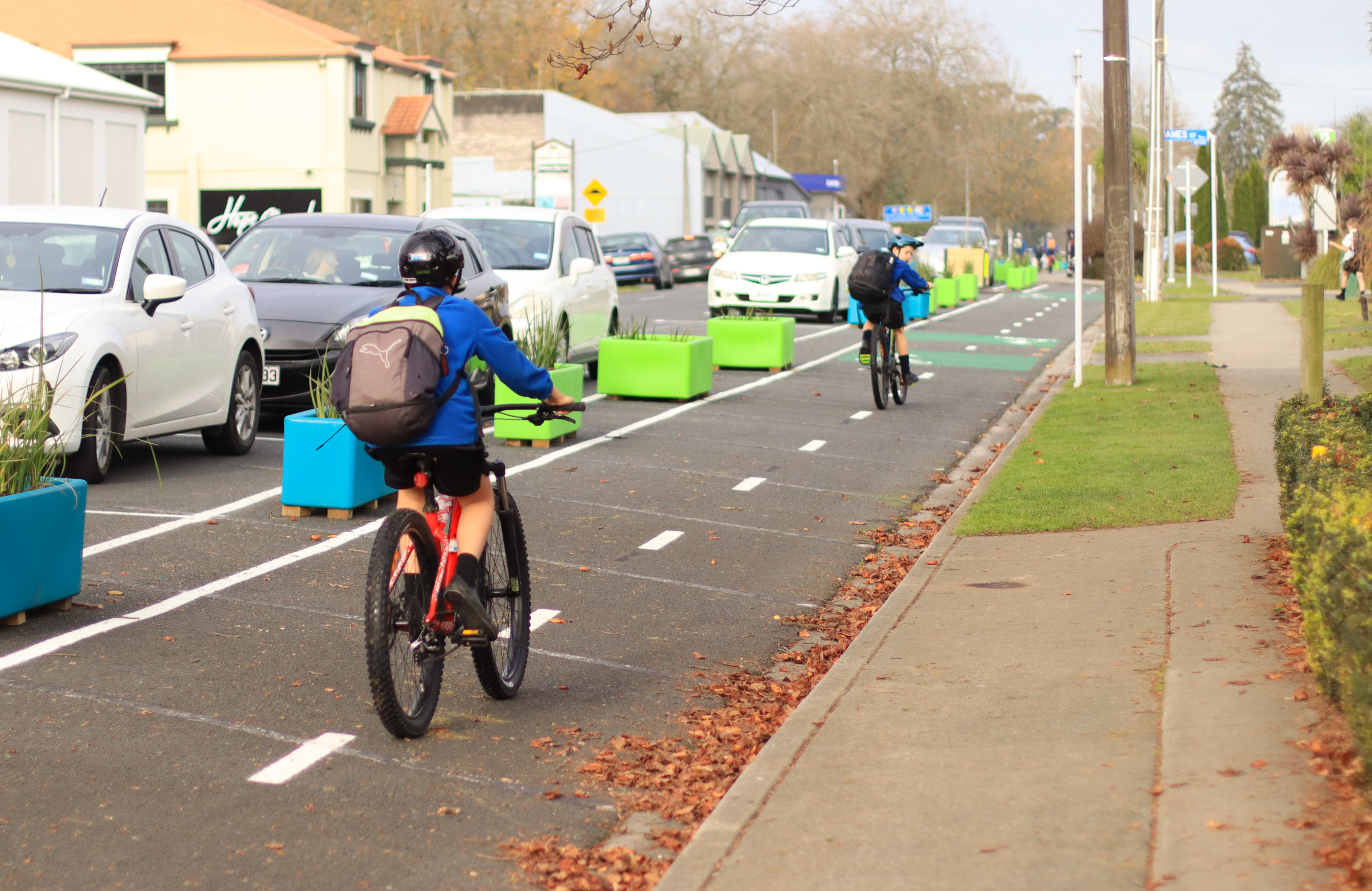 Two young people with safety gear biking on cycleway with planters on the side running parellel at a suburban street 