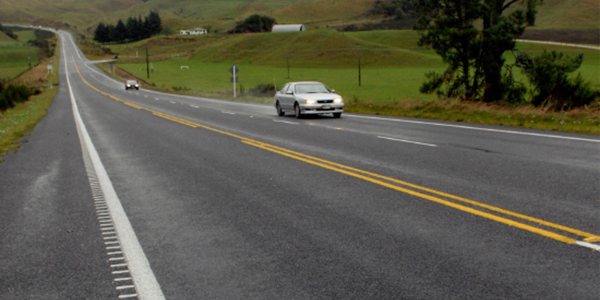A car driving along a rural road, the road has rumble strips (white raised lines) along the edges
