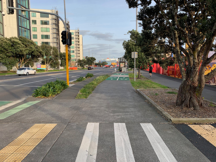 A cycleway is separated from the footpaths on either side by grass and trees. Vegetation also separates the road from a footpath.