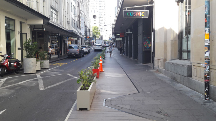A line of small concrete planter boxes separate the widened footpath from the road.