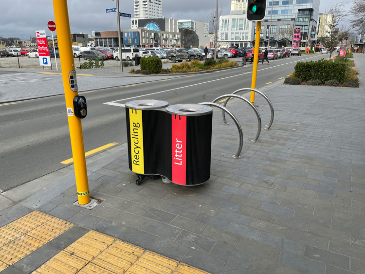 Rubbish and recycling bins between bike parking and a signalised pedestrian crossing.