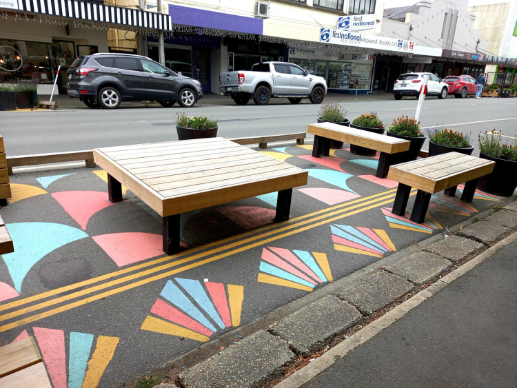Temporary parklet on previously on-street parking. The parklet has planter boxes, a variety of benches and vibrant geometric road paint.