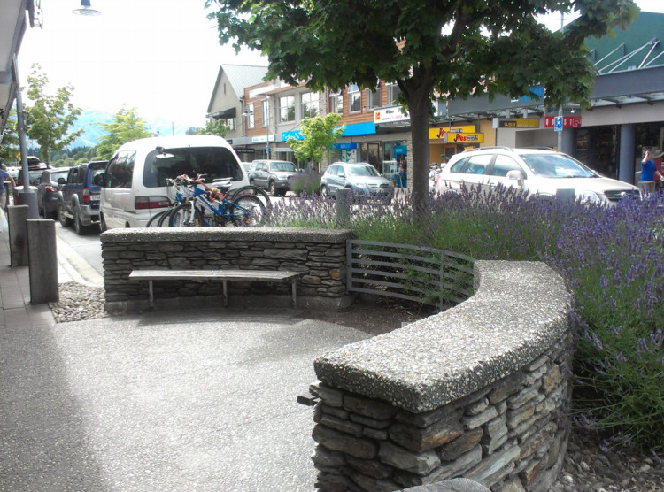 Public benches in a path buildout. The benches are against a curved wall with bushes and trees behind.