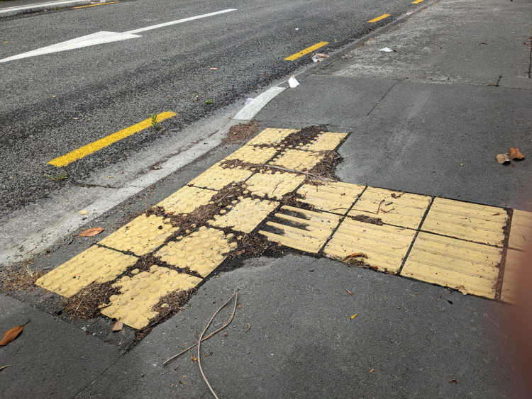 Yellow square by road with debris near tactile pavers, posing detection challenges.