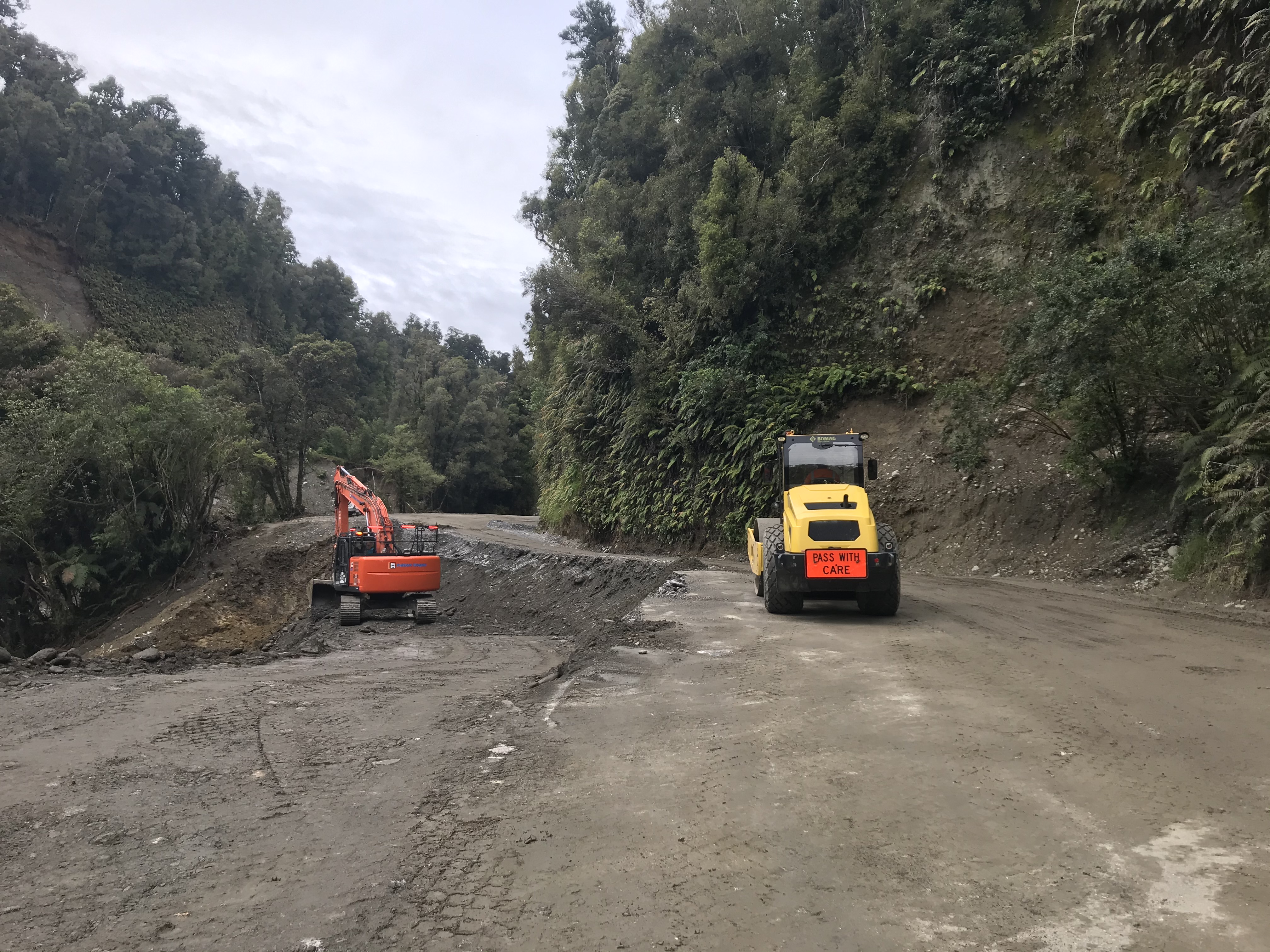 A yellow and orange digger work on the Haast highway on State Highway 6