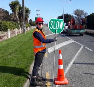 Person in safety gear holding a slow sign beside the road